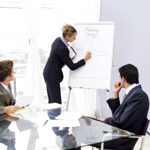 Businesswoman Writing on White Board and Businessman at Table